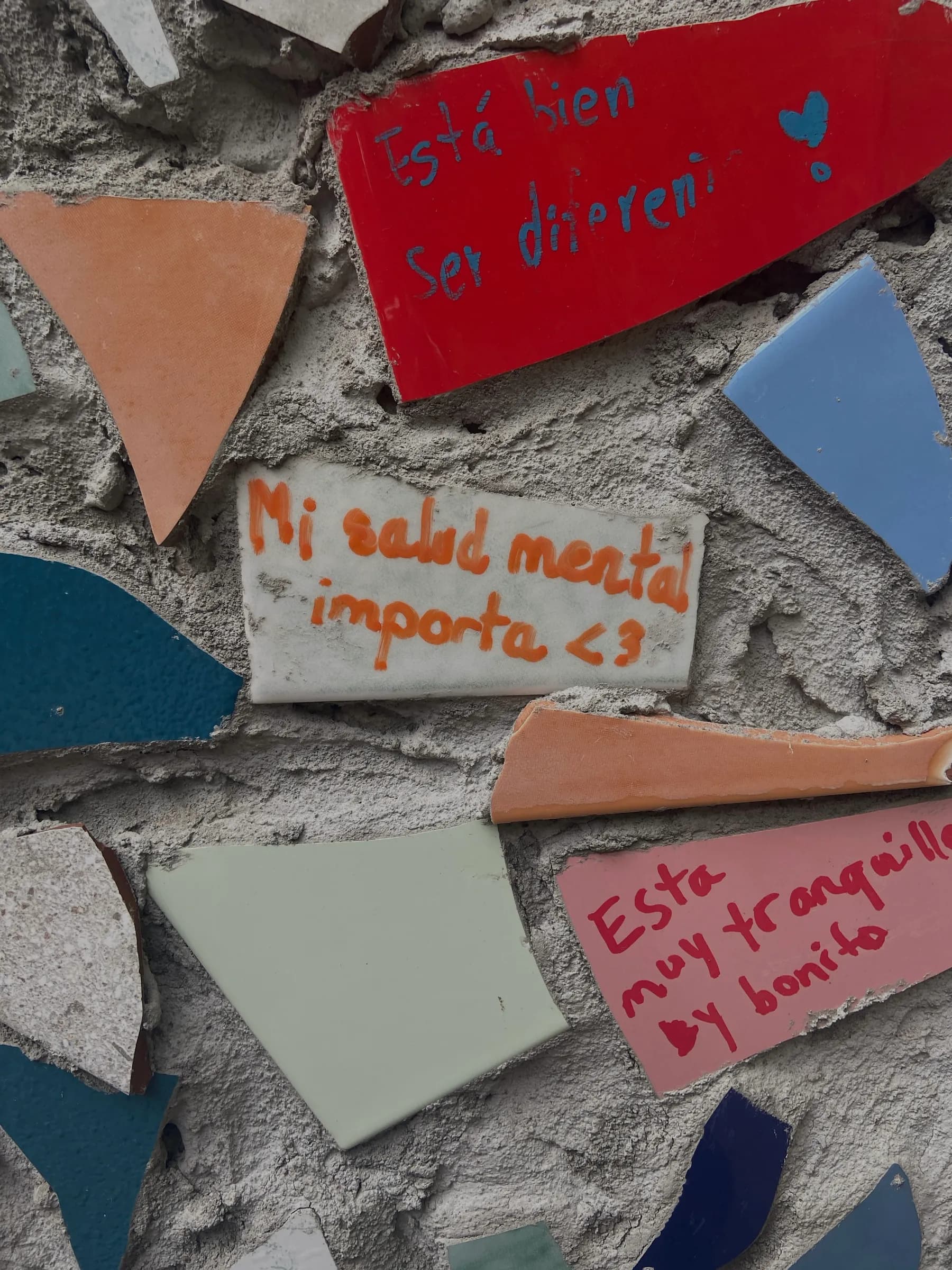 A mosaic wall covered in handwritten notes about mental health and self-acceptance, including 'mi salud mental importa'