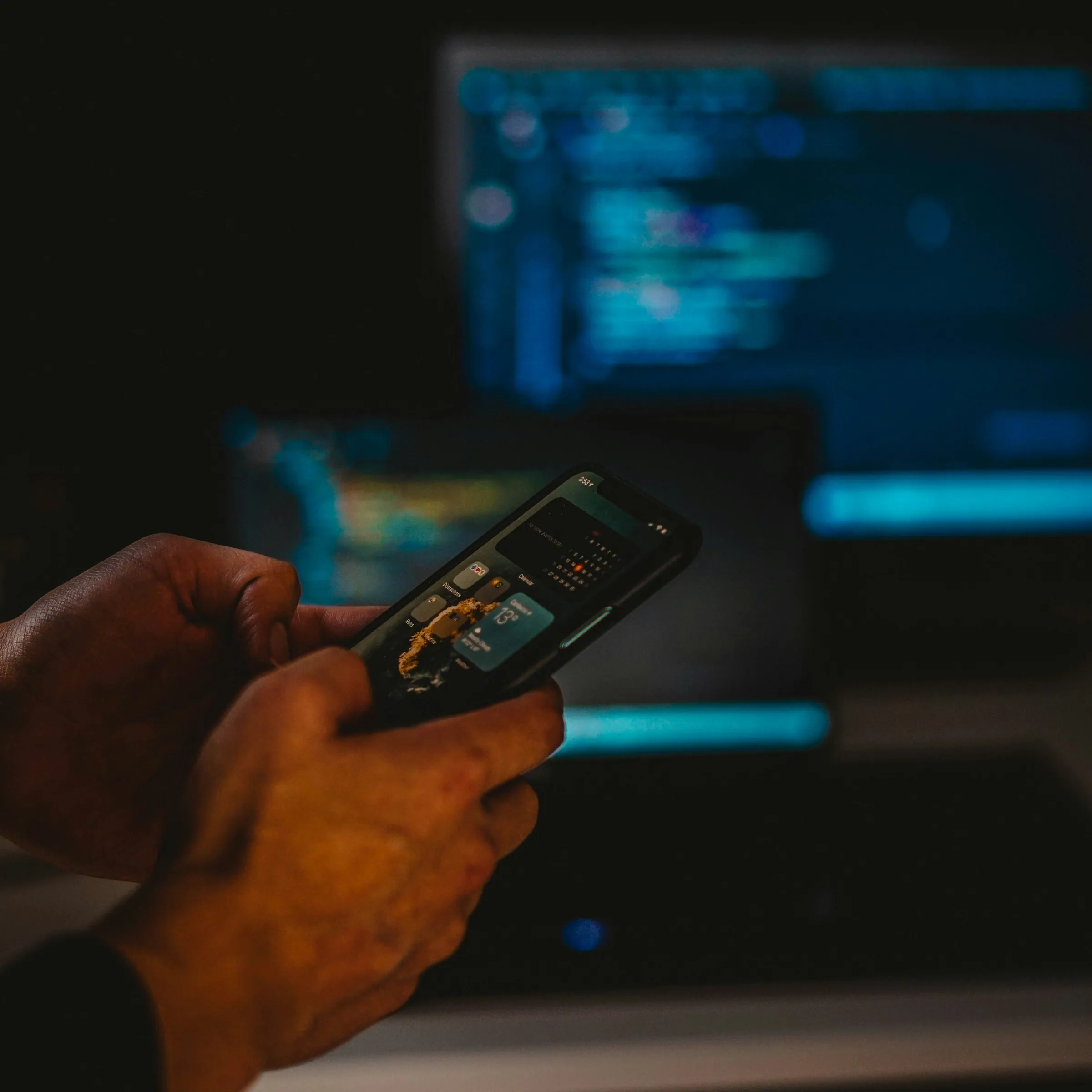 A hand holding a phone at night, screens and code glowing behind it